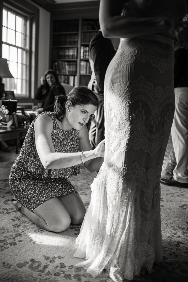 Friend adjusts train of bride's wedding dress during cocktail hour