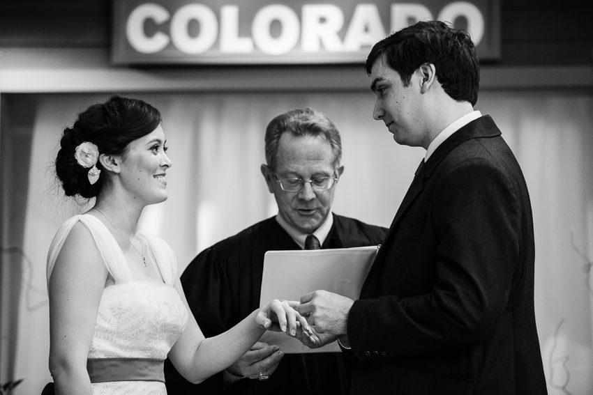 At a History Center Colorado wedding, groom places ring on bride's finger.