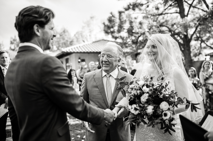During a wedding at The Villa Parker in Colorado, Denver wedding photojournalist depicts the groom and bride shaking hands immediately after her father walked her down the aisle.