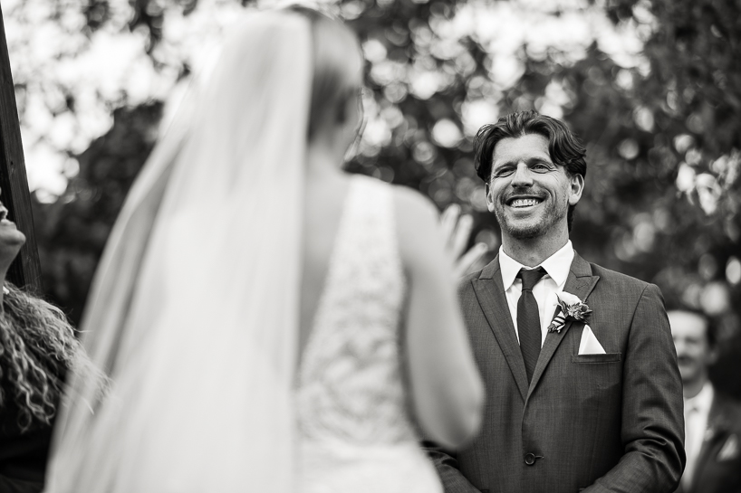 Denver photographer at The Villa Parker wedding depicts officiant and groom laughing at bride's remarks during the ceremony.