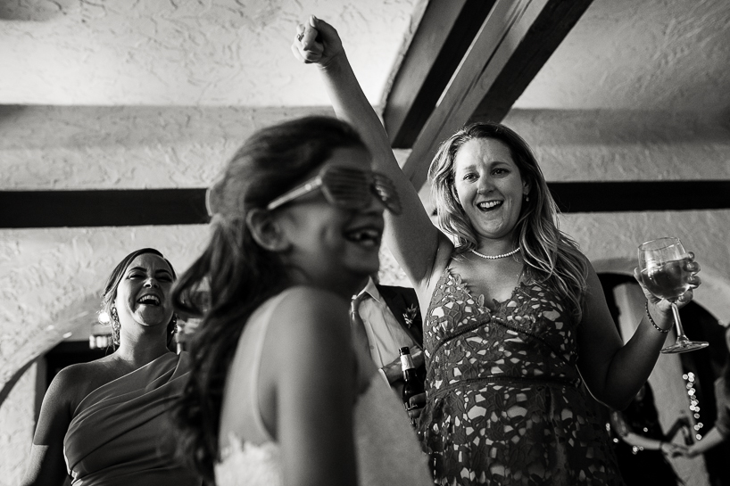 On a wedding dance floor, the young daughter of the groom is laughing while a woman with a wine glass cheers her. Picture made by Denver wedding photojournalist at The Villa Parker.