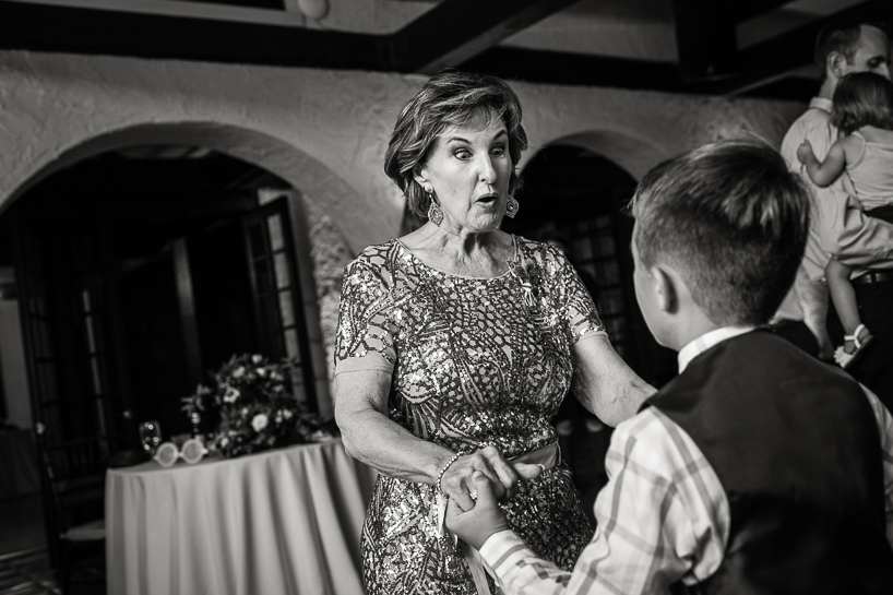 At a wedding reception, an older woman makes a crazy face at a young boy with whom she is dancing.