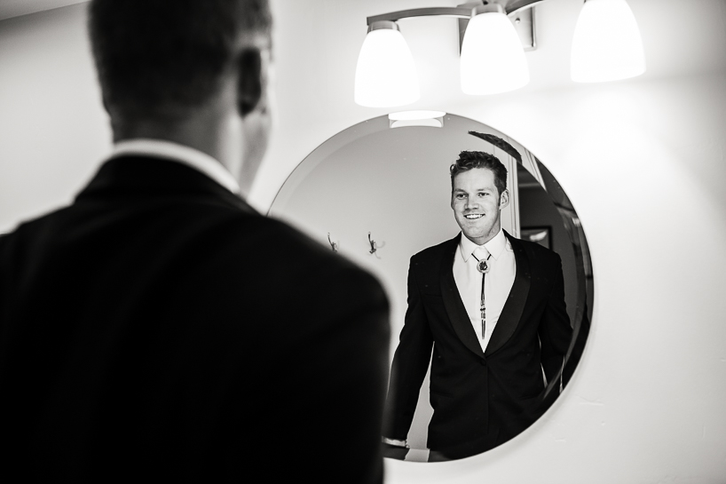 Groom views himself in mirror getting ready for Aspen wedding.