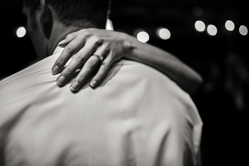 Candid image of bride's hand on groom's back, showing wedding ring.