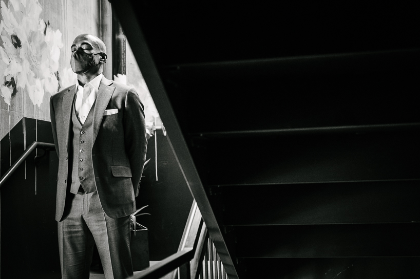 Groom with mask waits in stairwell before a wedding ceremony at The Ramble Hotel in Denver.