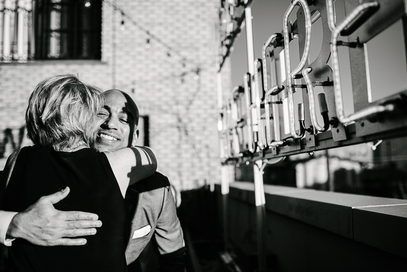 Groom embraces a friend on the rooftop terrace of The Ramble Hotel in Denver.
