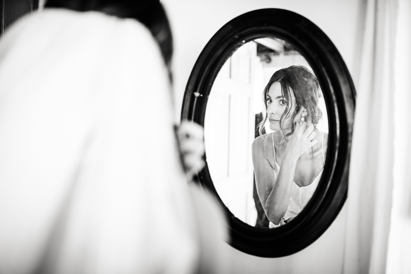 Bride puts on earrings in mirror in image by Denver wedding photographer.