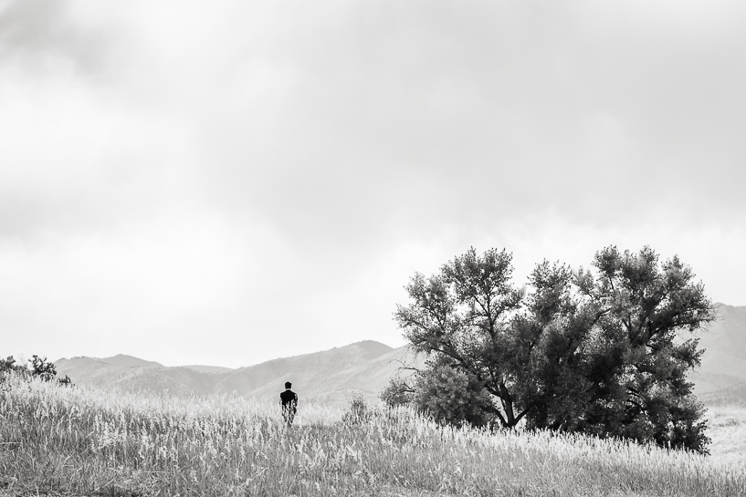 Man walks through open fields near mountain foothills as depicted by Denver wedding photographer.