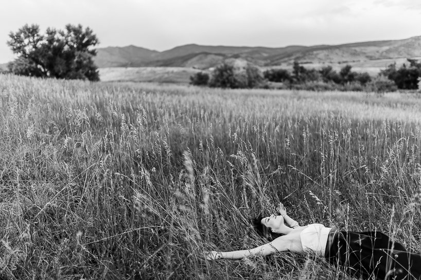 Woman lies in open field with arms outstretched in the early evening by Denver wedding photographer.