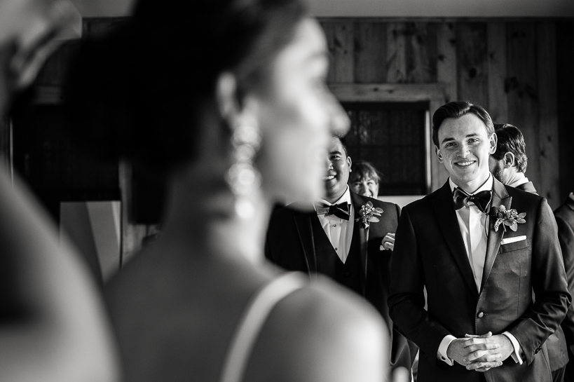A groom in a tuxedo watches his fiance get ready before their wedding.