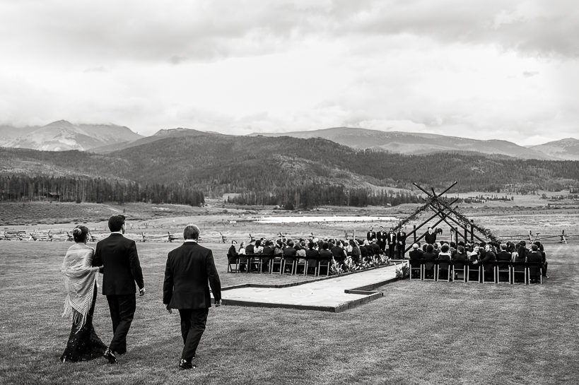 A groom is walked to the site of an outdoor ceremony on the Devil's Thumb Ranch wedding deck.