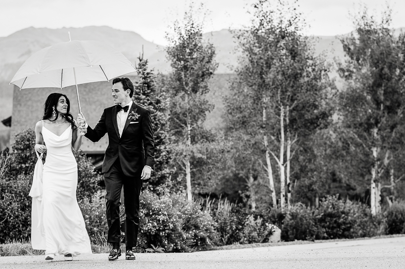 Bride and groom walk to wedding reception under an umbrella, Aspens and mountains in the background.