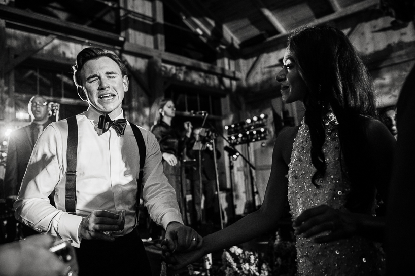 Black and white wedding photograph of groom and bride on dance floor, he in a pool of light, she in the shadows, as he sings.