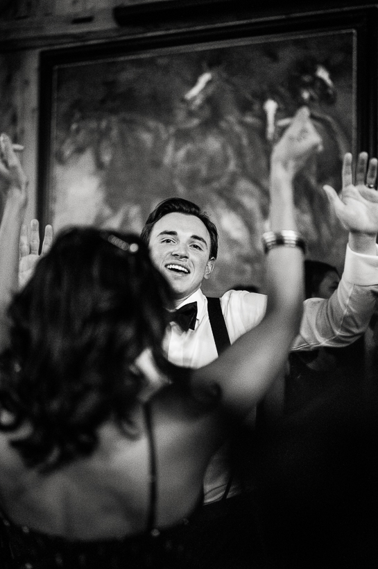 Groom in a Devil's Thumb Ranch wedding reception, his hands in the air, dancing, as seen through the up stretched arm of woman in the foreground.