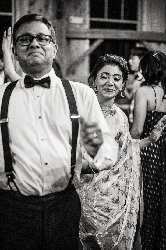 Man in suspenders and bow tie smiling while woman in sari laughs behind him.