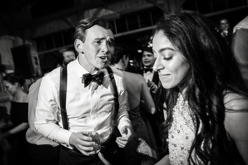 Groom croons to bride on dance floor in a black and white wedding photo with dramatic lighting.
